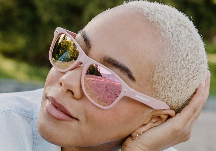 Woman wearing pink smirror BioSunnies sunglasses with a blurred outdoor background