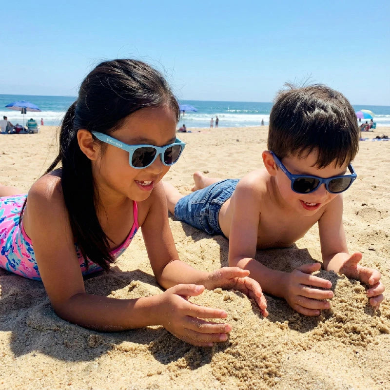 Two children playing in the sand on a beach with BioSunnies sunglasses on.